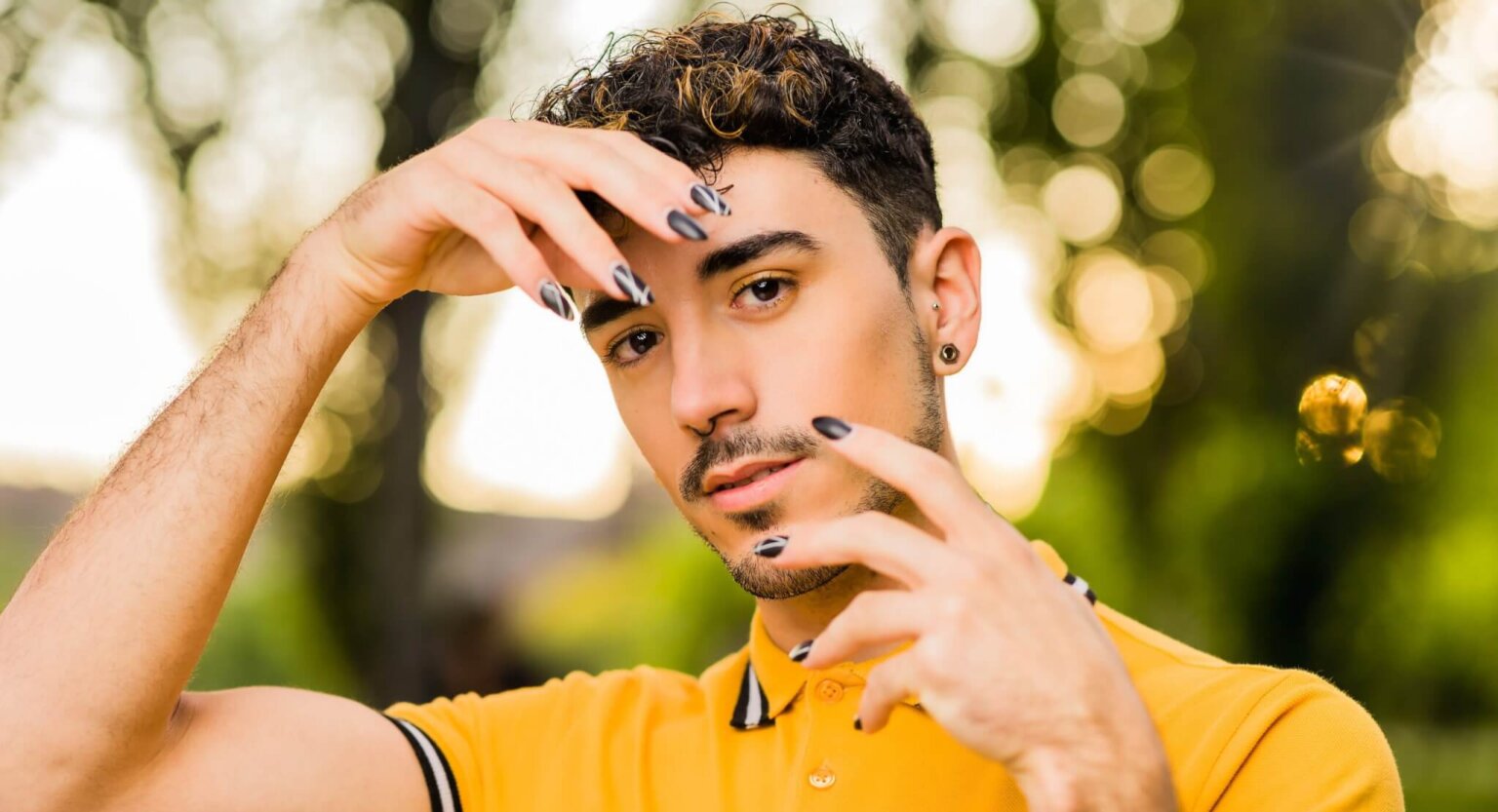 Man in yellow top with black nail polish on