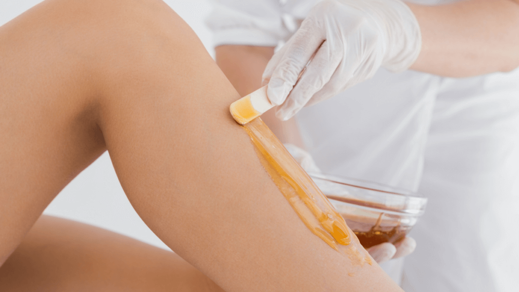 An image of a beautician applying was onto a woman's legs