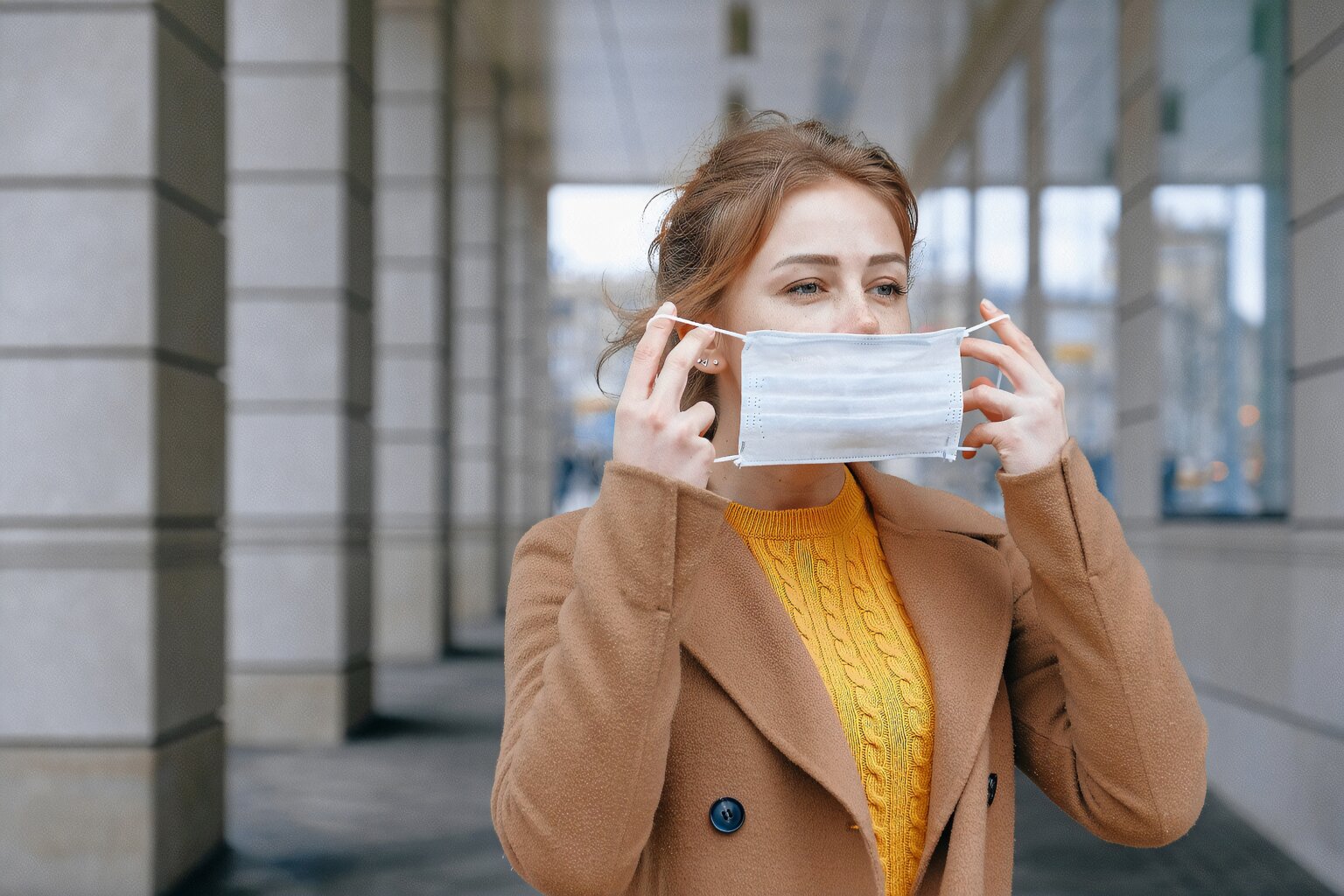 lady with light brown coat putting on face mask