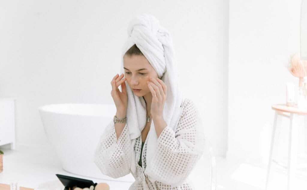 lady with towel on her had applying cream to her face as part of a skincare regime